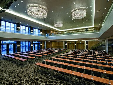 Modern hall at Maritim Hotel Düsseldorf with row seating, large windows, and impressive chandeliers.