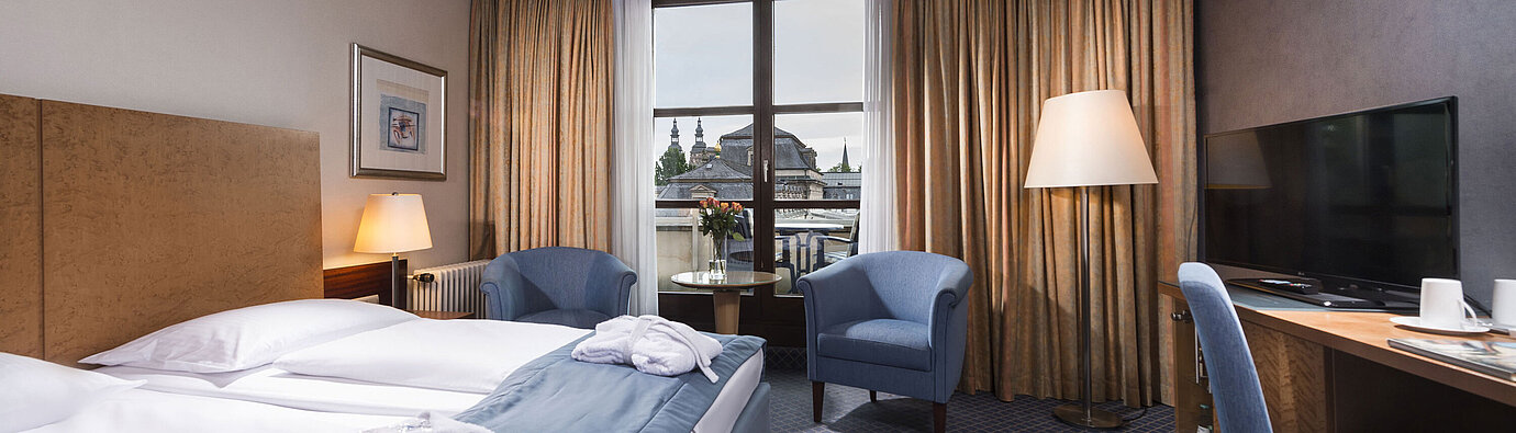 Elegant superior room at Maritim Hotel Fulda with double bed, seating area, and balcony overlooking the city.