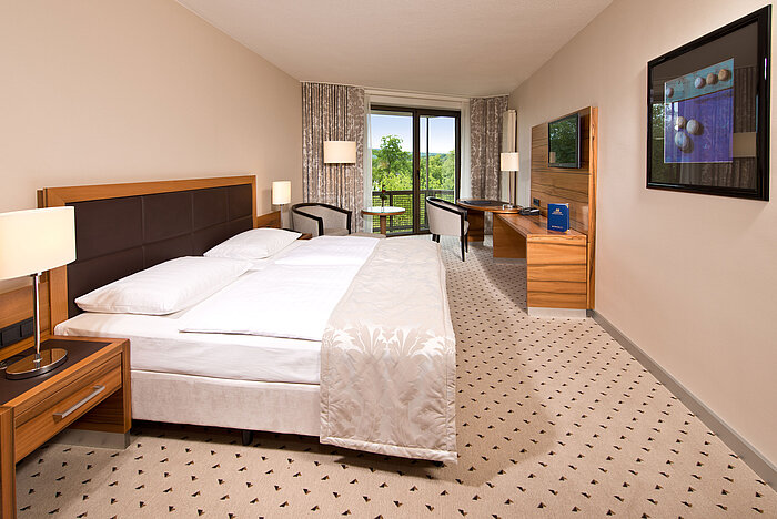 Bright room at Maritim Hotel Bad Homburg with cozy bed, desk, and balcony with green view.