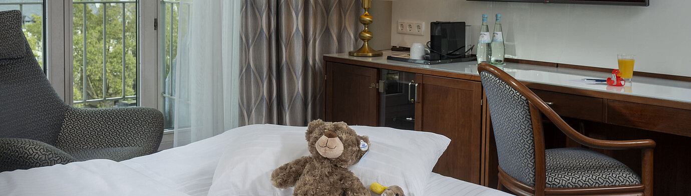 Family suite Family room at the Maritim Hotel Cologne with TV, cozy stuffed animals on the bed, and a view of the Rhine.