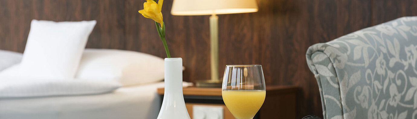 Details of a room at the Maritim Hotel Kiel: glass of orange juice, headphones and vase on the table, a bed in the background.