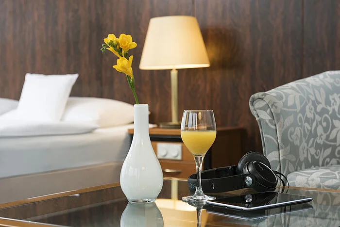 Details of a room at the Maritim Hotel Kiel: glass of orange juice, headphones and vase on the table, a bed in the background.