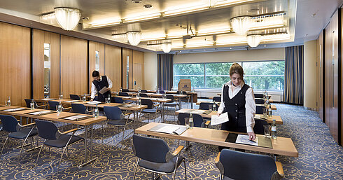Staff preparing a conference room at Maritim Hotel Frankfurt with row seating and views of greenery.