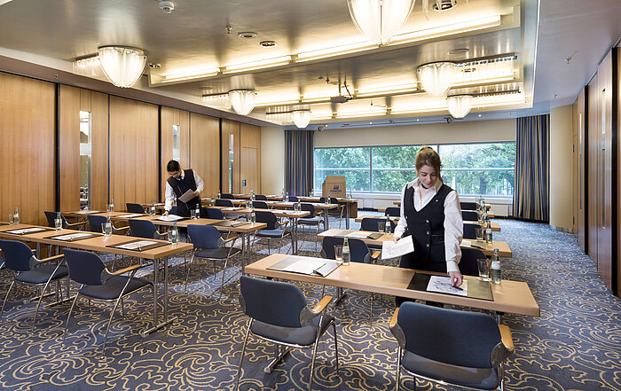 Staff preparing a conference room at Maritim Hotel Frankfurt with row seating and views of greenery.