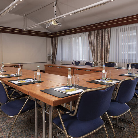 Modern conference room at the Maritim Hotel Magdeburg with U-shaped seating, natural light, and high-quality equipment.
