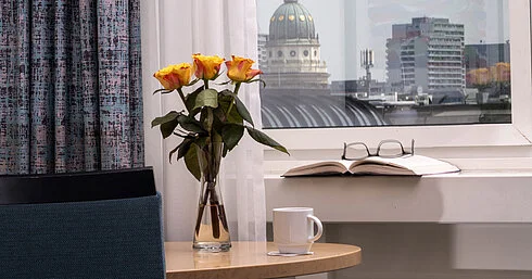 Vase with yellow roses, book and cup by window overlooking Französischer Dom at Maritim proArte Hotel Berlin