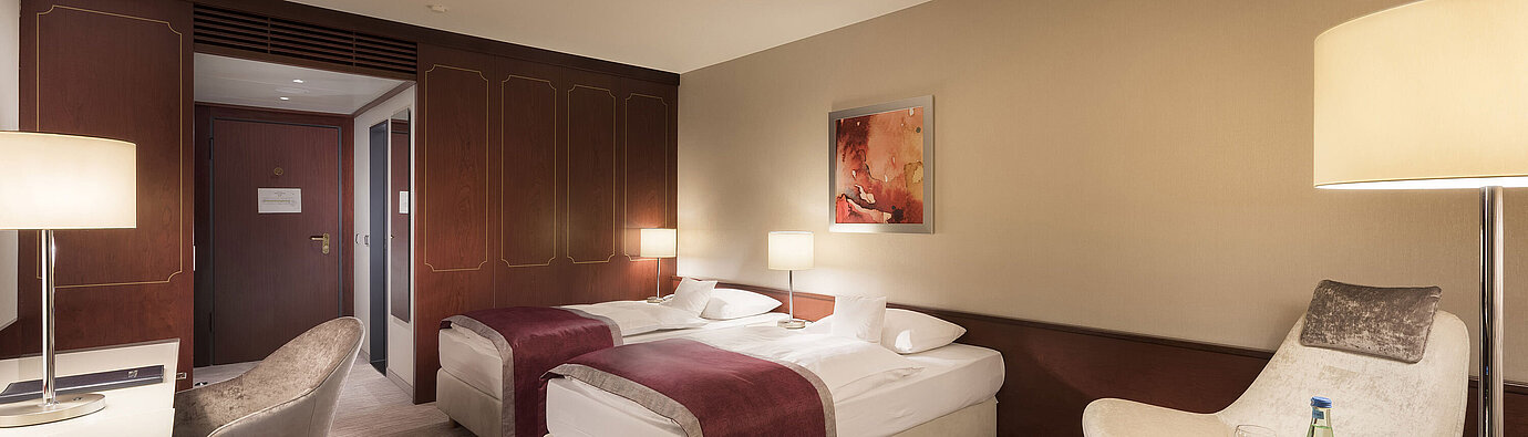 Comfort room at Maritim Hotel Bonn, featuring two single beds, armchair, desk, and modern lighting.