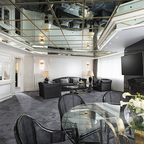 Stylish living room of the luxury suite at Maritim Hotel Bonn with mirrored ceiling, modern furniture, and large dining table.