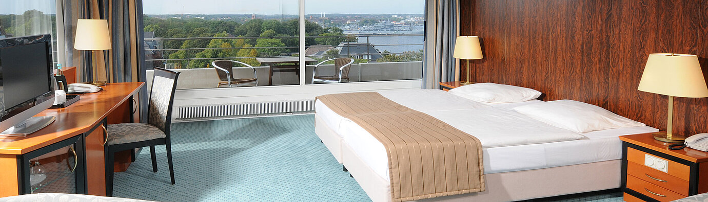 Comfort room Spacious hotel room with a double bed, seating area and wide views of Kiel through the large window front.