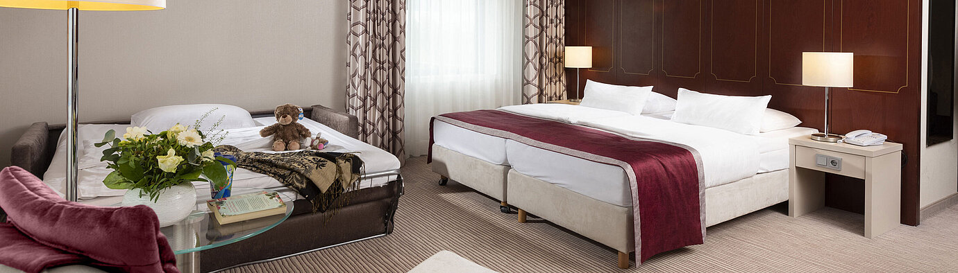 Comfort family room at Maritim Hotel Bonn with a large double bed, pull-out sofa, armchair, and flower arrangement.
