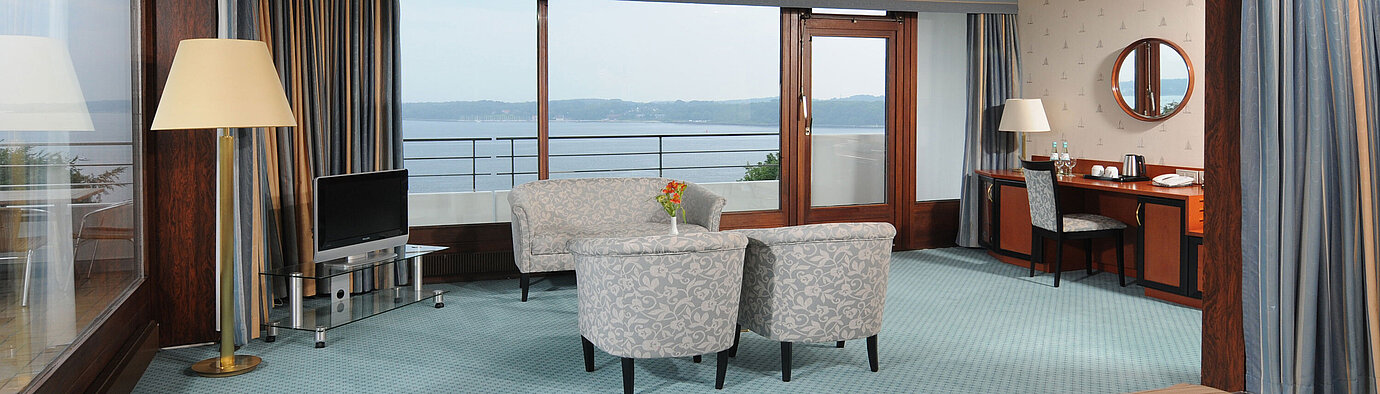 Junior suite Junior Suite in the Maritim Hotel Kiel, with sitting area, desk, TV and large window front with sea view.