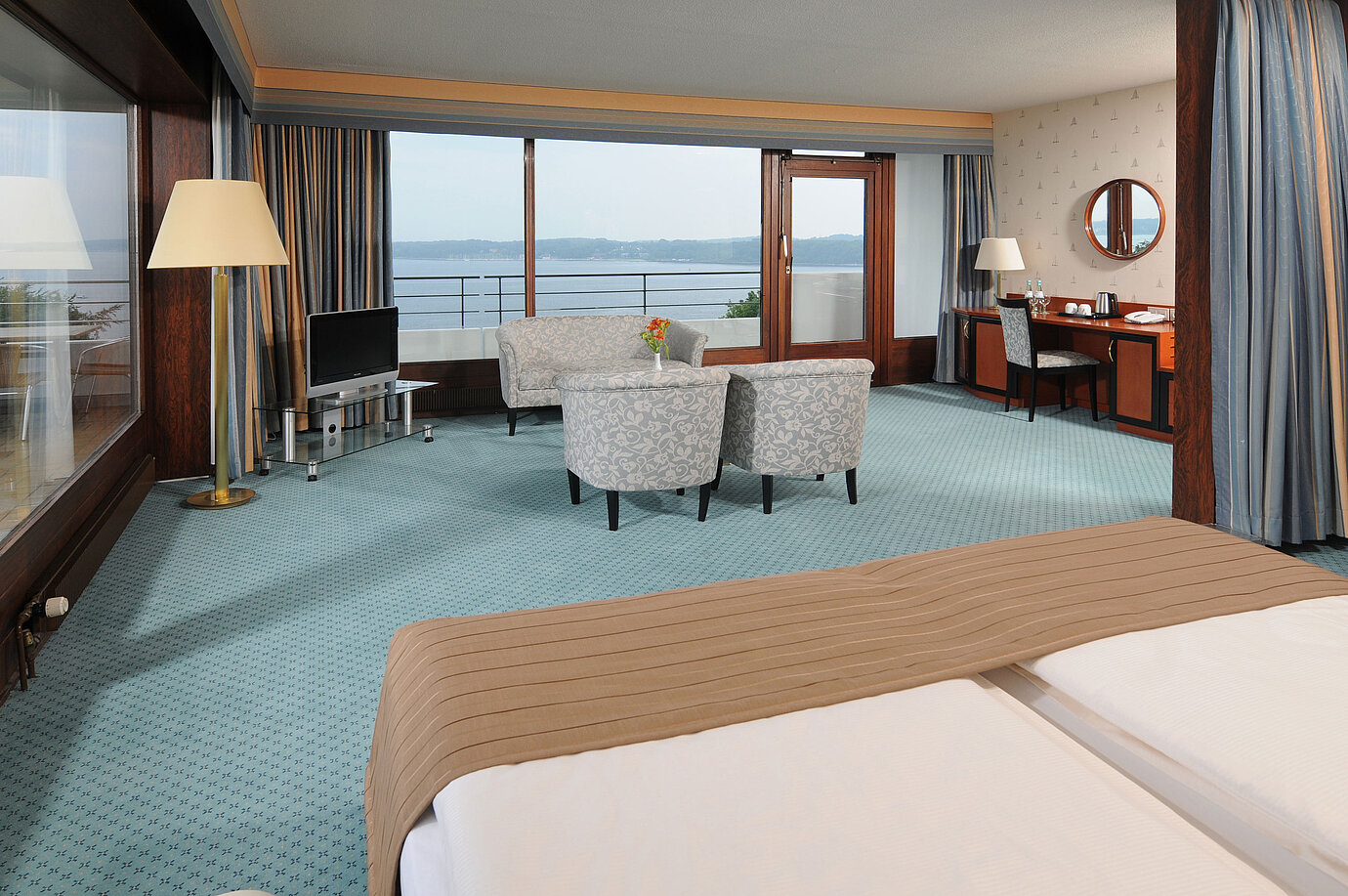 Junior Suite in the Maritim Hotel Kiel, with sitting area, desk, TV and large window front with sea view.