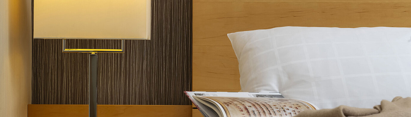 Close-up of a bedside table at Maritim Hotel Düsseldorf with a lamp, glass of water, and book on a bed.