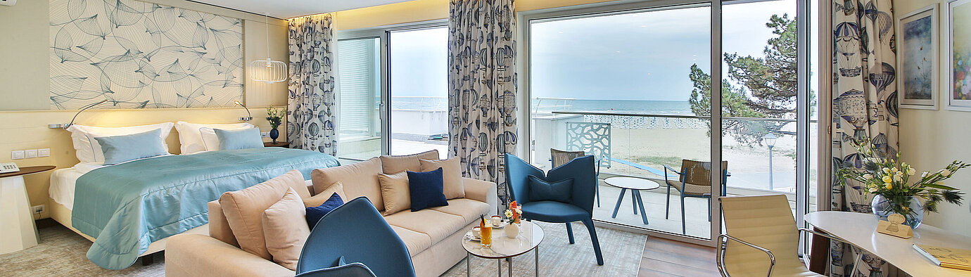 Suite with large bed, seating area and balcony with sea view in a modern hotel