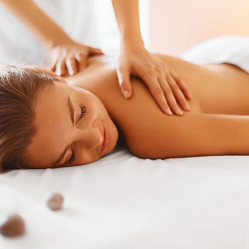 © puhhha - AdobeStock.com Woman enjoying relaxing back massage in spa with warm light and stones