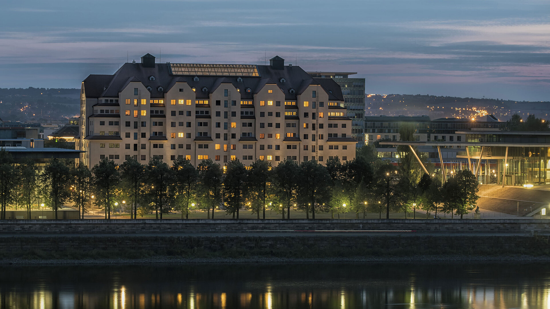 Exterior view at night Illuminated Maritim Hotel Dresden at dusk with lights reflecting on the Elbe River.