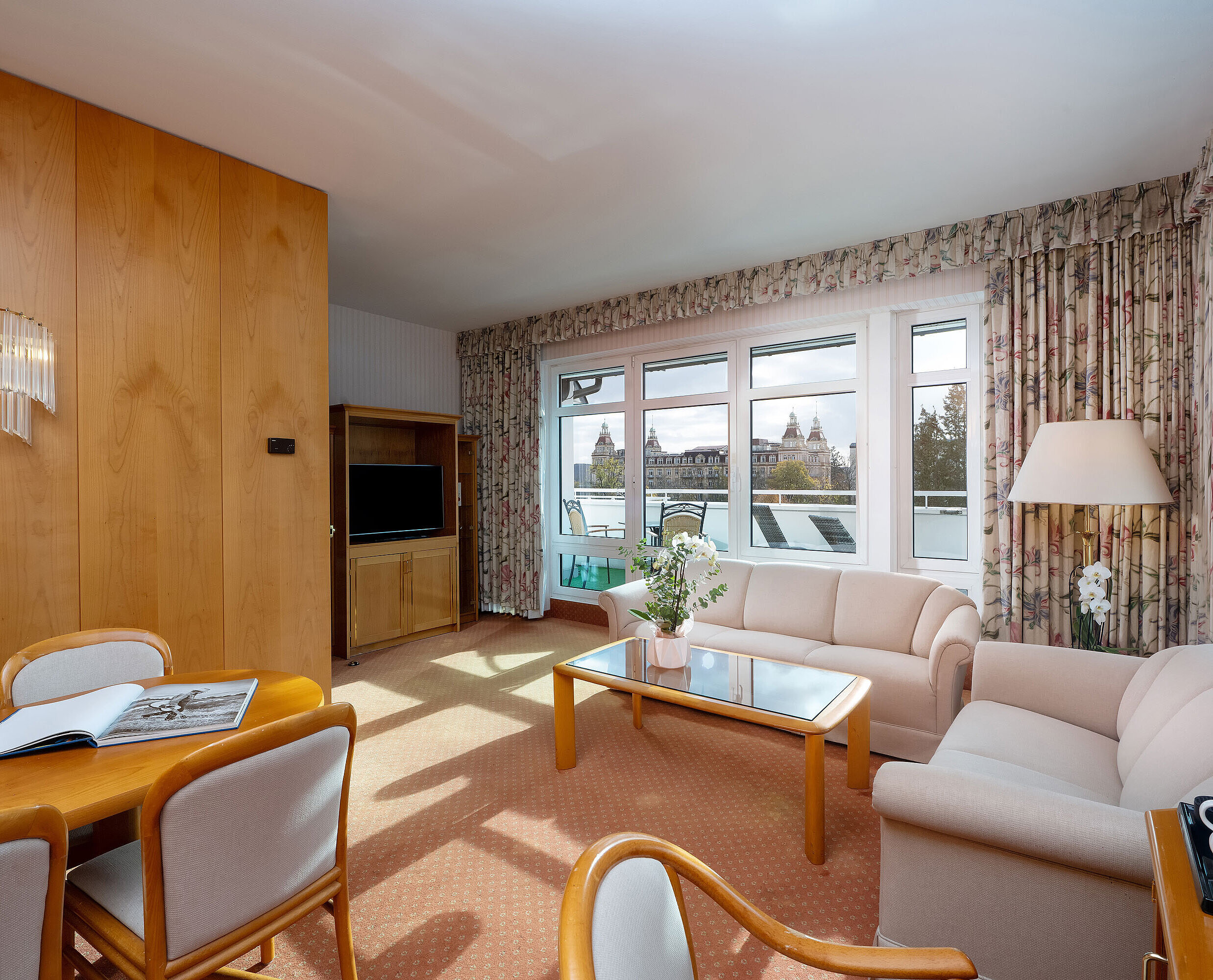 Junior Suite with bright living area, sofa, large window, dining space and classic interior at the Maritim Hotel.