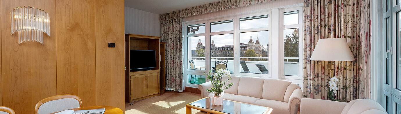 Junior Suite with bright living area, sofa, large window, dining space and classic interior at the Maritim Hotel.