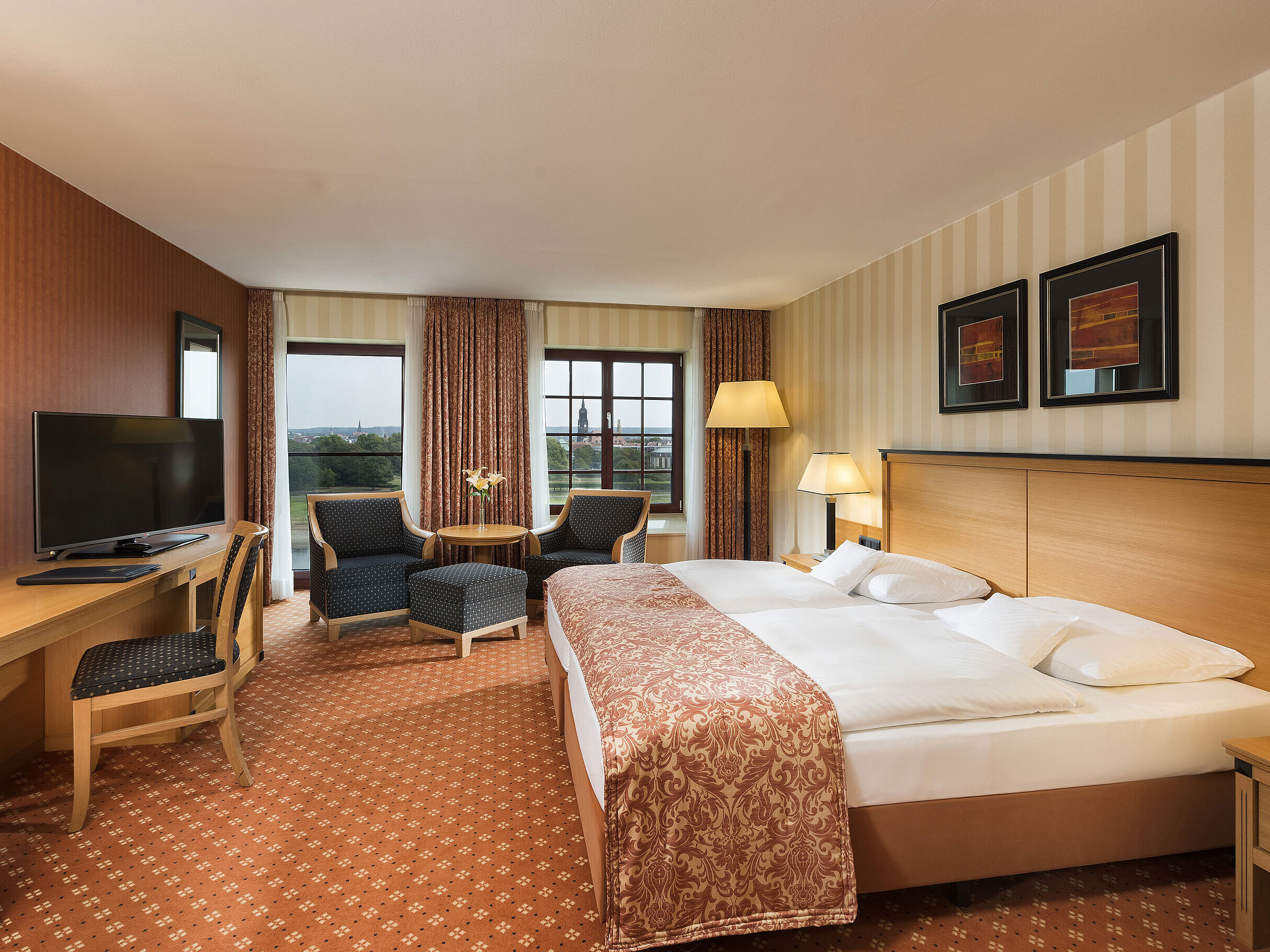 Superior room at Maritim Hotel Dresden with elegant double bed, desk, and seating area with city view.
