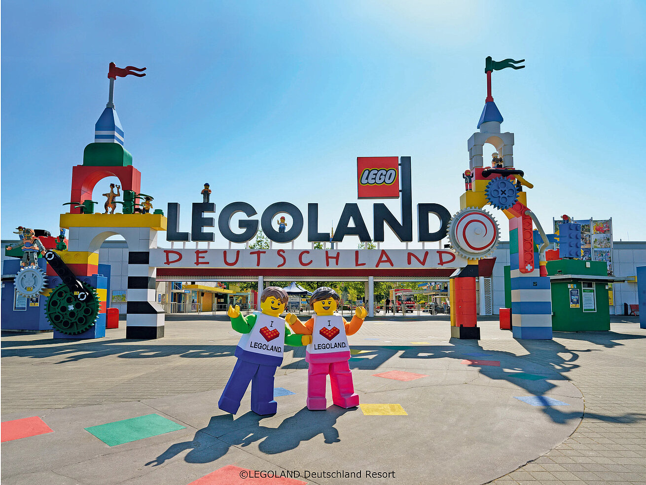 Colorful entrance of LEGOLAND® Deutschland Resort with giant LEGO® figures and blue sky.