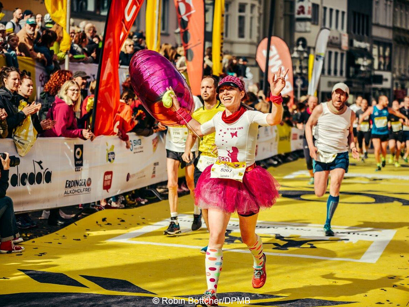 Deutsche Post Marathon Female runner in pink outfit celebrates crossing the finish line at a city marathon