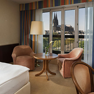 Superior room at Maritim Hotel Cologne featuring a seating area, comfortable bed, and view of Cologne Cathedral.