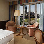 Superior room at Maritim Hotel Cologne featuring a seating area, comfortable bed, and view of Cologne Cathedral.
