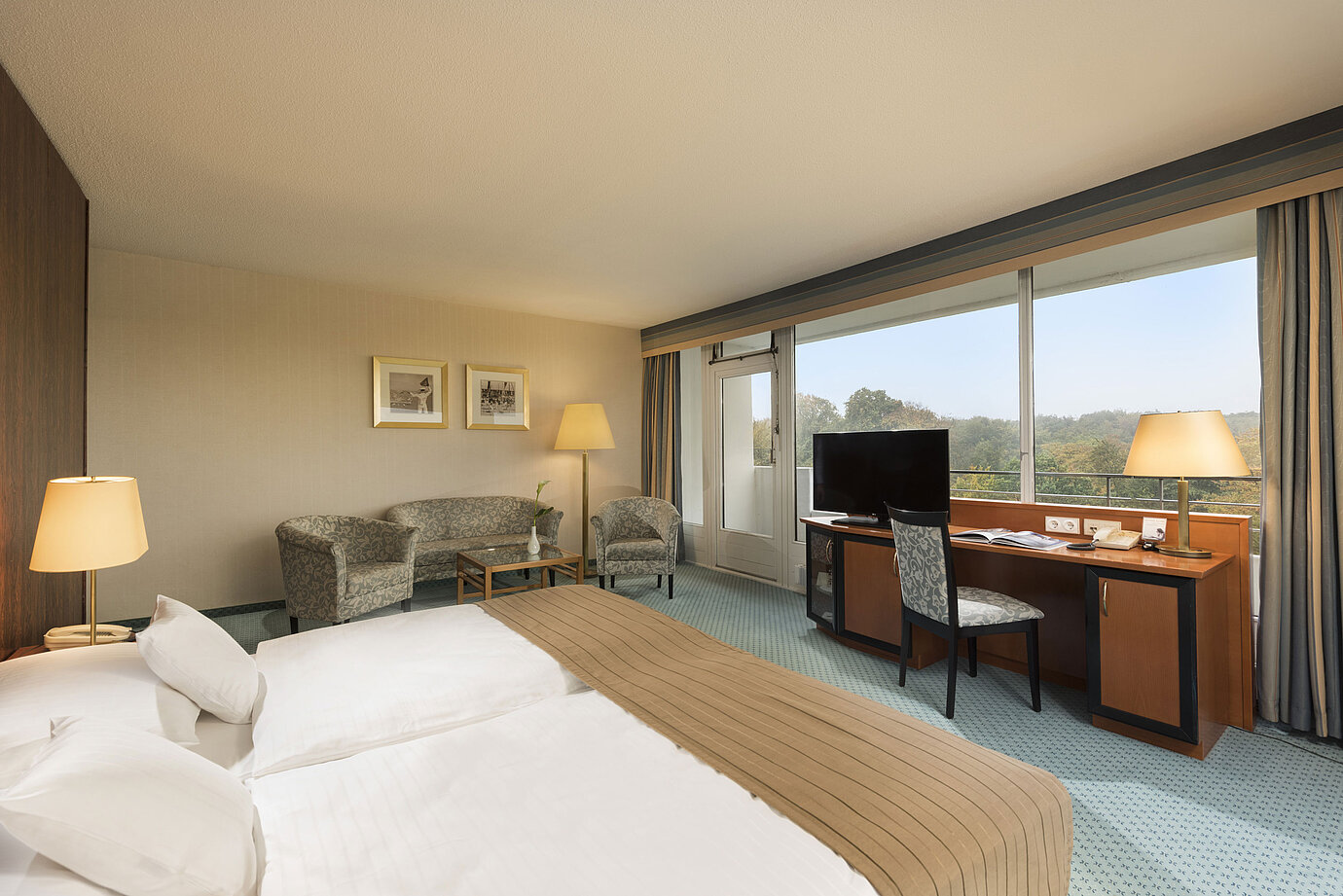 Comfort room at the Maritim Hotel Kiel with a cozy seating area, desk, large bed and a wonderful view of the countryside.