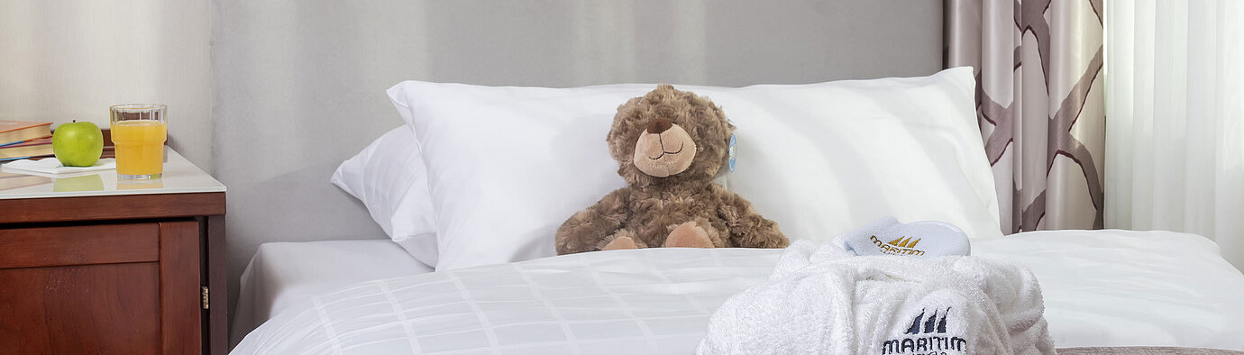 Family suite at the Maritim Hotel Bonn featuring a cozy bed, stuffed toys, and a bathrobe, perfect for kids.