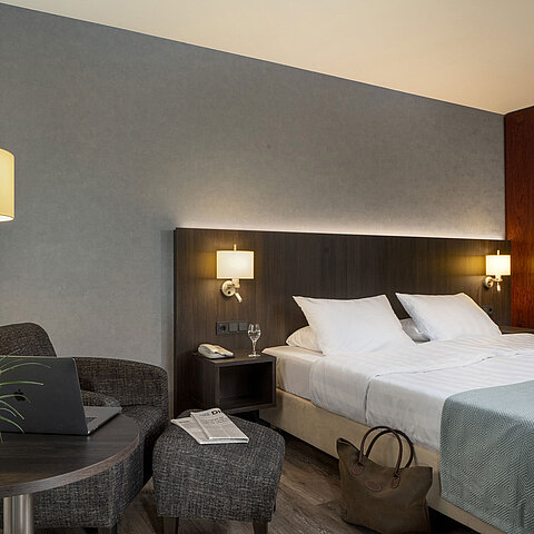 Modern double room at Maritim Hotel Bremen with cozy seating area, side table, vase, and inviting bed.