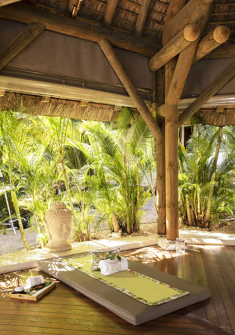 Outdoor spa lounger in lush greenery with Buddha statue, wooden floor and tropical plants