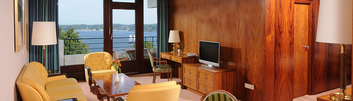 Junior Suite in the Maritim Hotel Kiel, cozy sitting area, desk, TV and balcony with a view of the water.