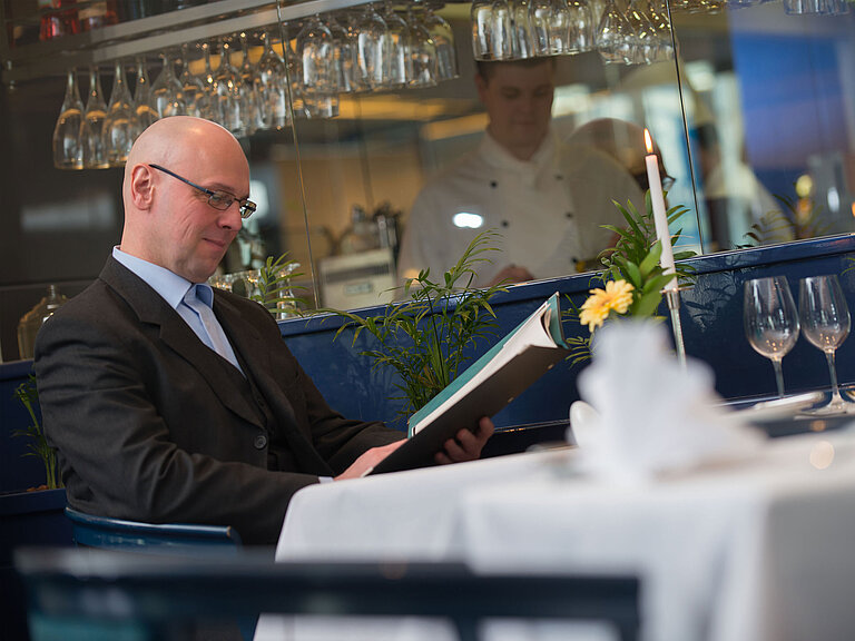 Restaurant Elegant set table in the restaurant of Maritim Hotel Magdeburg with a guest looking at the menu.