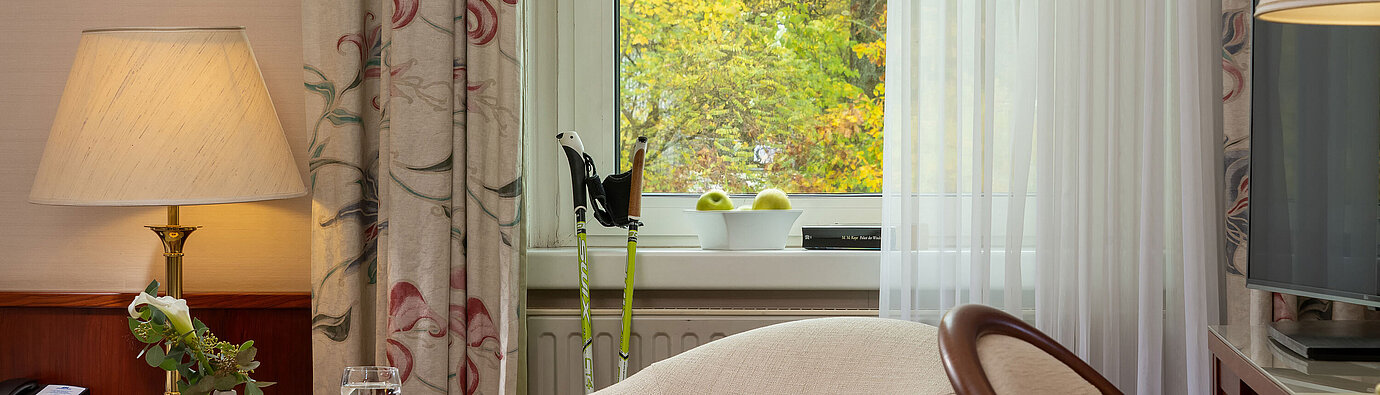 Seating area in the classic single room with armchair, table, lamp and window view at Maritim Hotel Bad Wildungen.