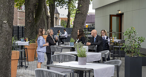 Modern terrace at Maritim Hotel Darmstadt with guests relaxing, trees in the background, and stylish gray furniture.