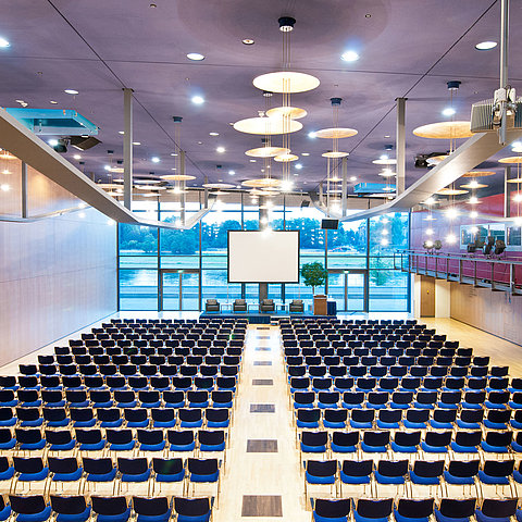 Large conference hall in Maritim Hotel Dresden with rows of blue chairs and a view of the Elbe River.