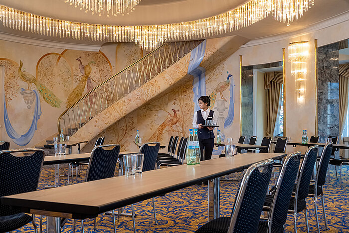 Fürst-von-Pückler Hall with row seating, artistic wall design, large staircase and a staff member in the room.