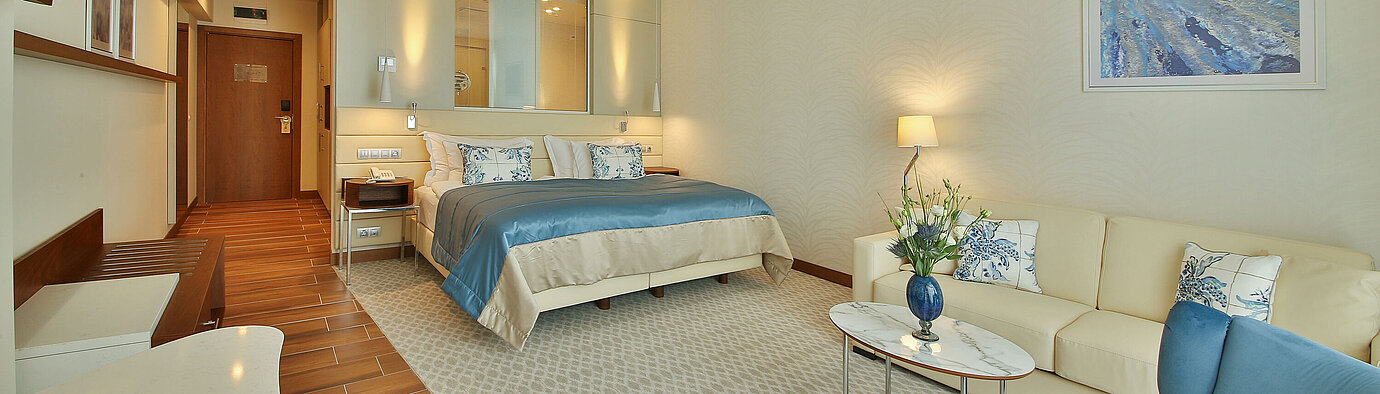 Spacious hotel room with double bed, seating area and modern interior in warm colours