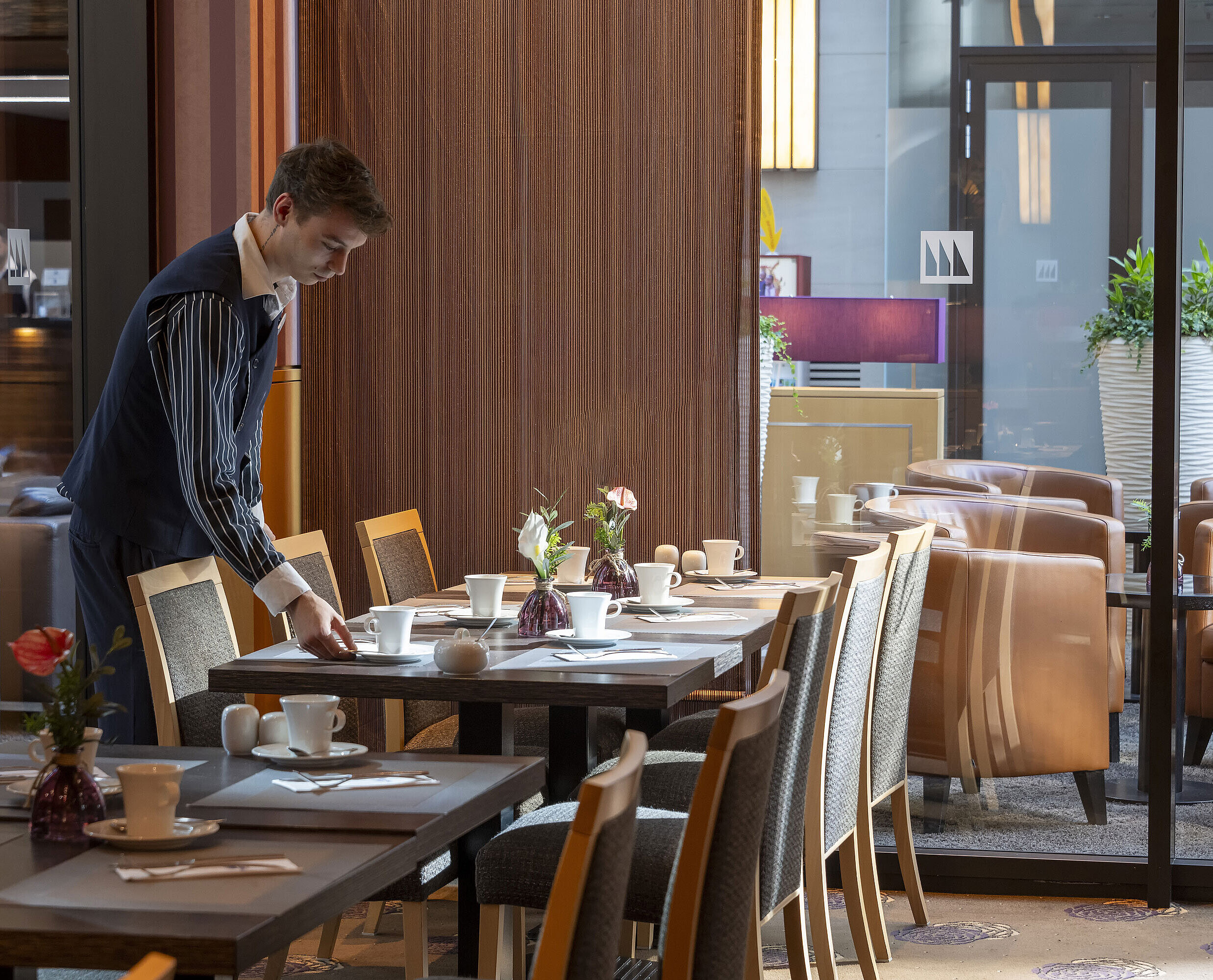 Classico Restaurant Staff member sets a table in the Classico restaurant of Maritim Hotel Düsseldorf, surrounded by elegant decor.