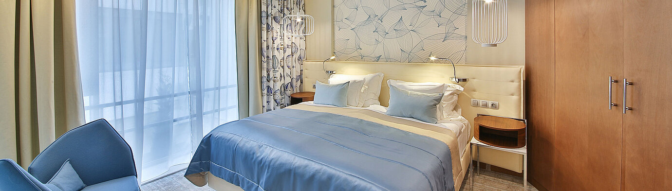 Modern hotel room with double bed, blue accents and large windows with curtains