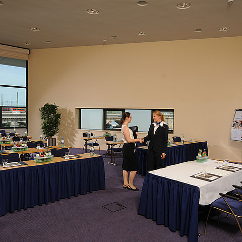 Bright meeting room in Maritim Hotel Dresden with set tables, flipchart, and two people shaking hands.