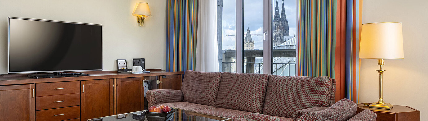 Senior Suite Living room of Senior Suite at Maritim Hotel Köln with sofa, TV, and Cologne Cathedral view through the windows.