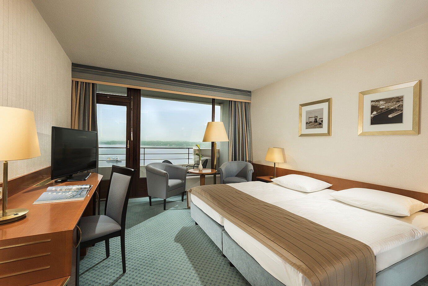 Superior room at the Maritim Hotel Kiel with desk, seating area, large double bed and balcony overlooking the fjord.