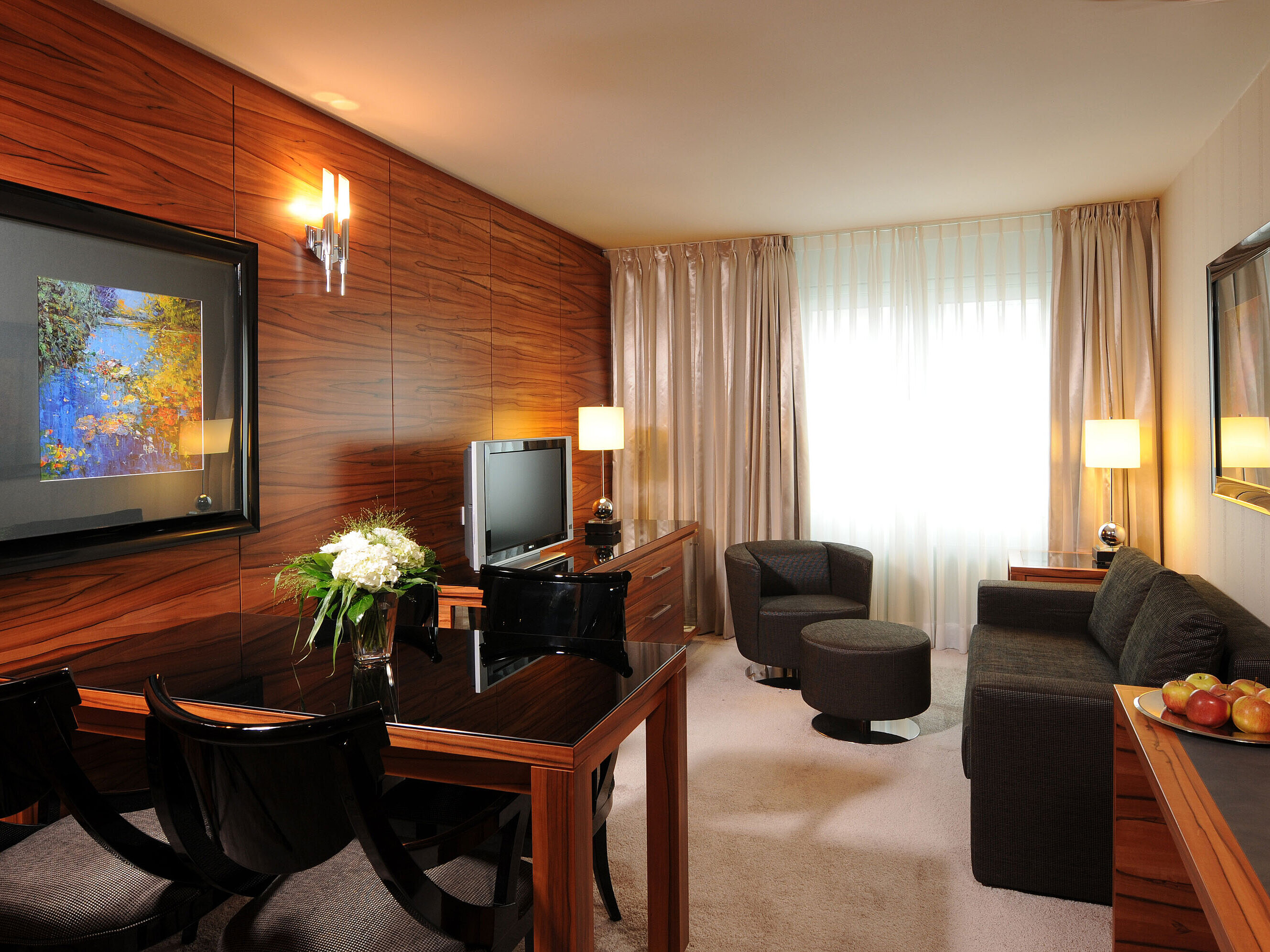 Bright living space with sofa, armchair, TV and desk at Maritim Hotel Munich