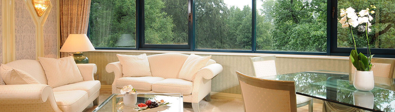 Suite Luxurious Suite with elegant seating, glass dining table, and large panoramic window with greenery view.