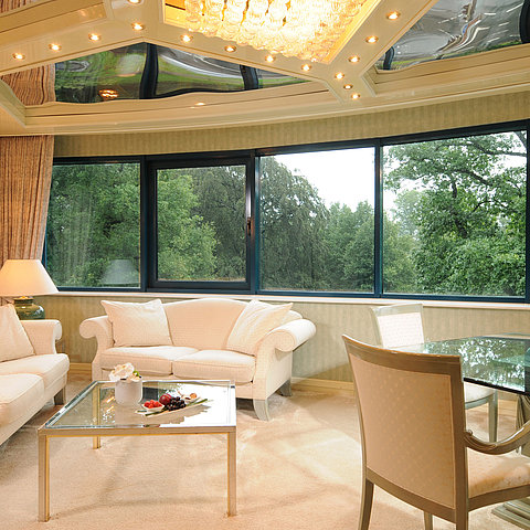 Luxurious Junior Suitewith elegant seating, glass dining table, and large panoramic window with greenery view.