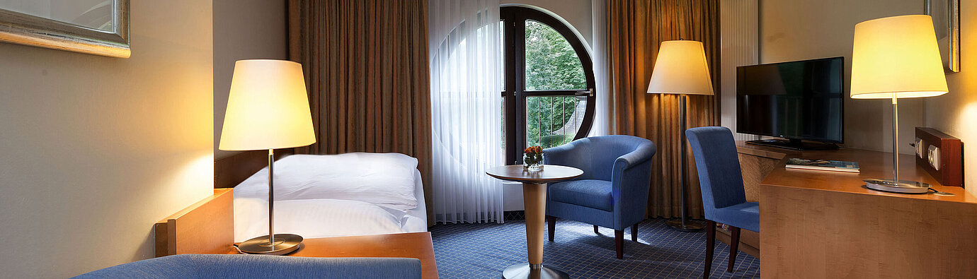 Classic room Classic room at Maritim Hotel Fulda with single bed, desk, seating area, and round window with a view.