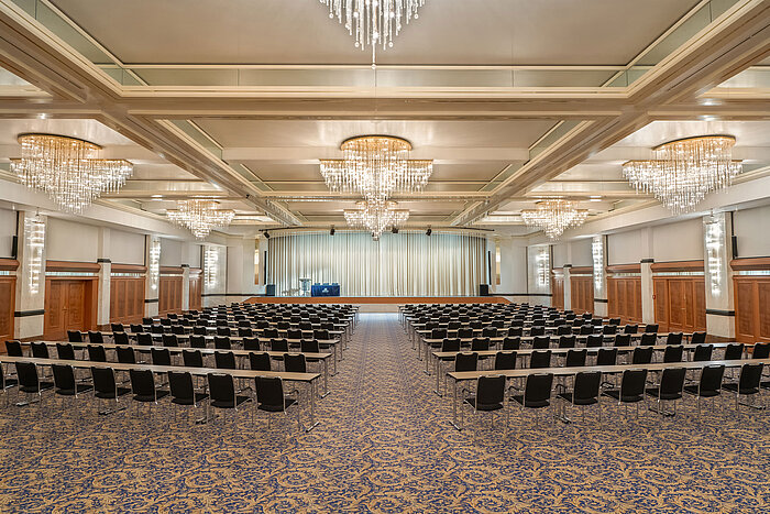 Salle Fürst-von-Metternich avec grande scène, rangées de sièges, lustres élégants et ambiance lumineuse.