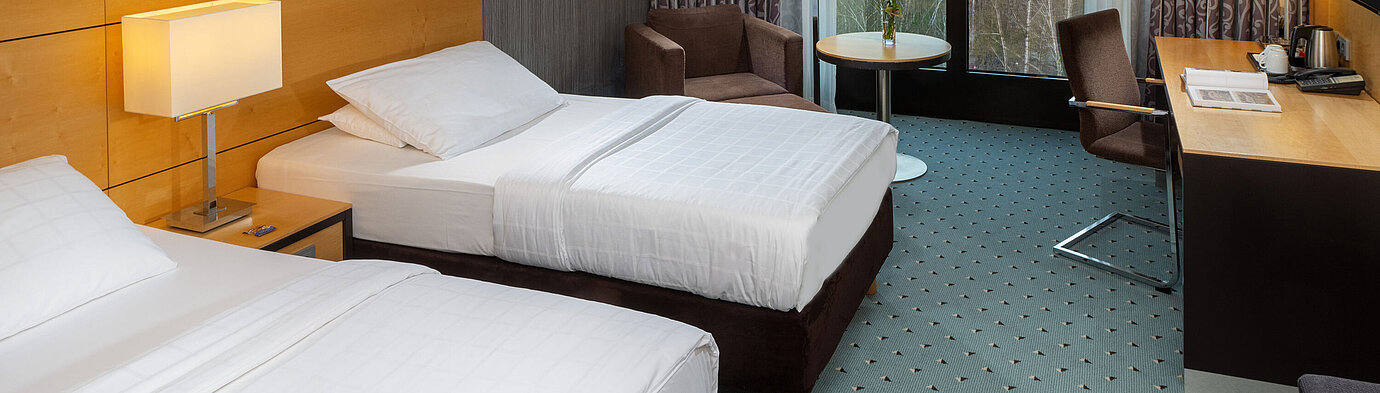 Classic room at Maritim Hotel Düsseldorf with two single beds, desk, armchair, and panoramic window overlooking the airport.