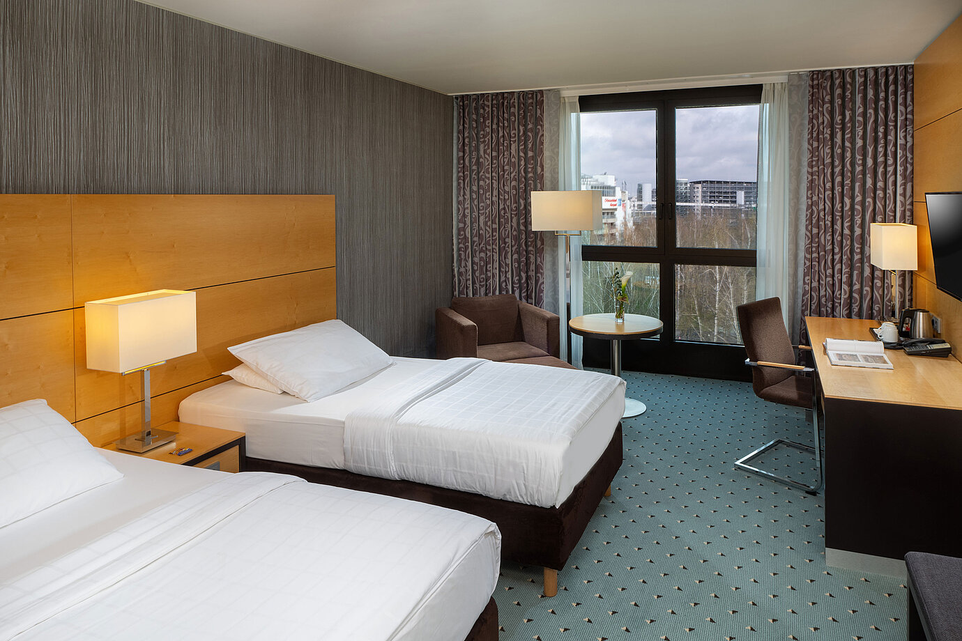 Classic room at Maritim Hotel Düsseldorf with two single beds, desk, armchair, and panoramic window overlooking the airport.